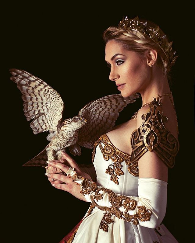 a beautiful woman in a white dress holding an owl on her arm and wearing a tiara