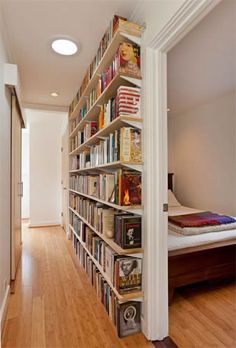 a book shelf in the corner of a room next to a bed with lots of books on it