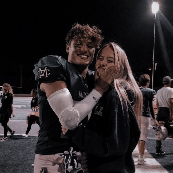 a man and woman hugging each other in front of a football field with lights on