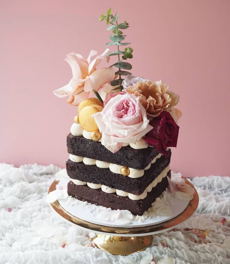 a piece of chocolate cake with flowers on top sitting on a table next to a pink wall