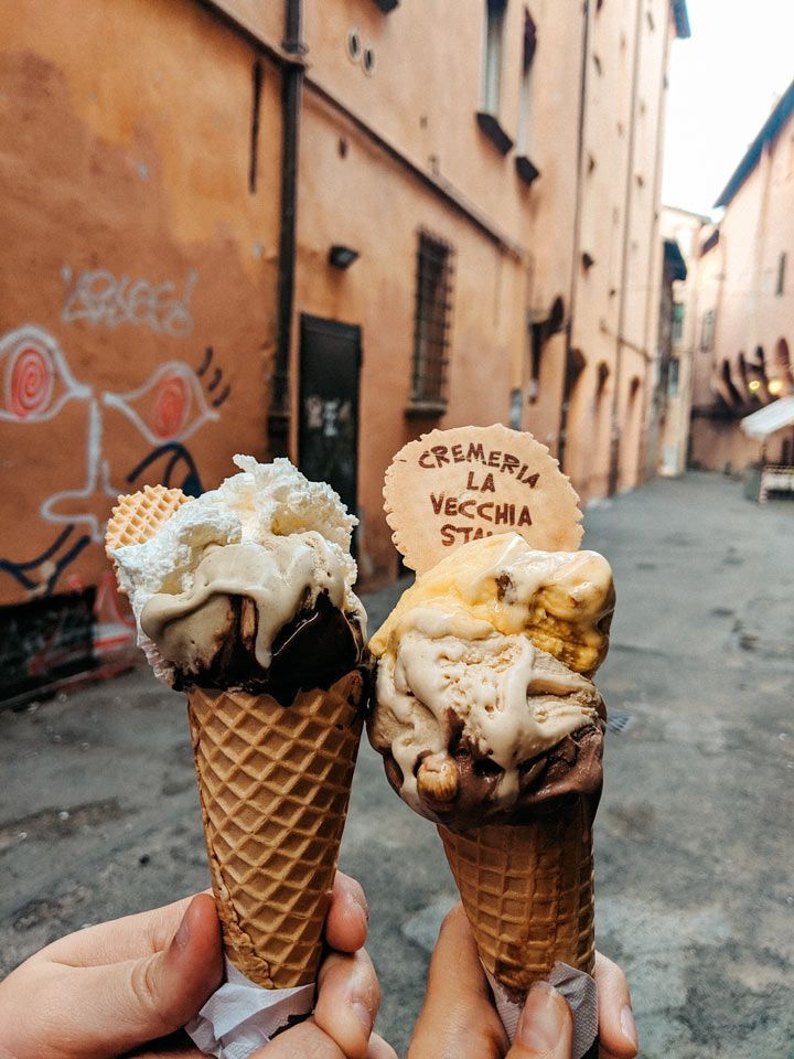 two people holding ice cream cones in front of an alleyway with graffiti on it