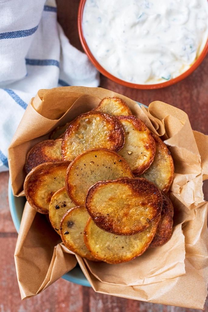 some fried potatoes are on a plate next to a bowl of yogurt and a napkin