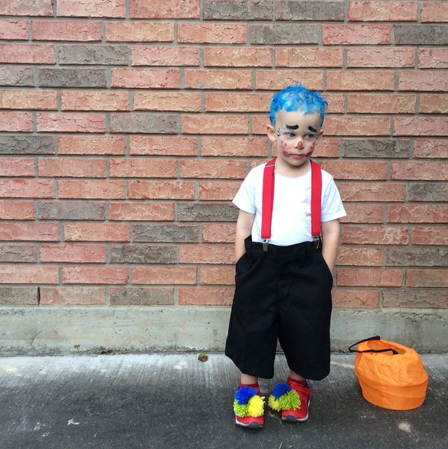 a little boy with blue hair and suspenders standing in front of a brick wall