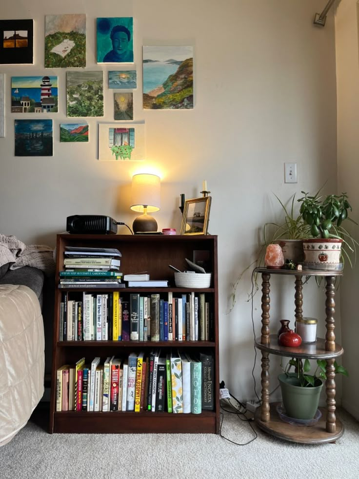 a bookshelf filled with lots of books next to a lamp and pictures on the wall