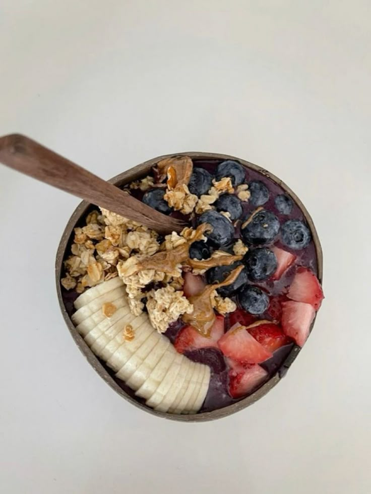 a bowl filled with fruit and granola on top of a white table next to a wooden spoon