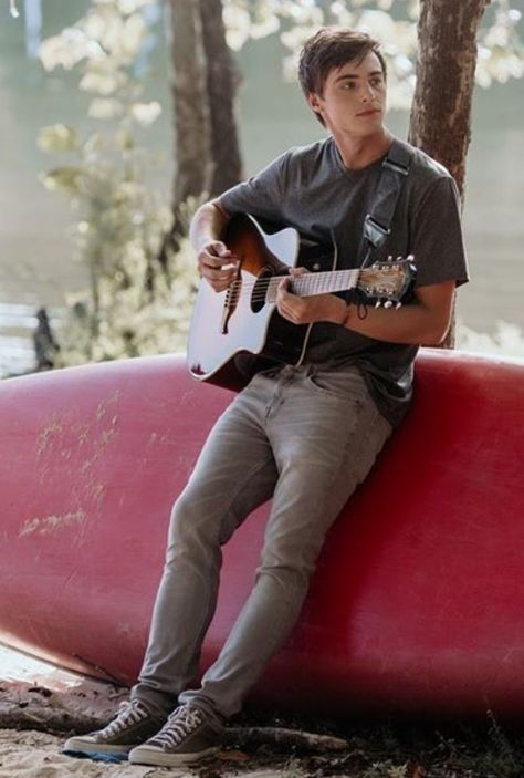 a young man sitting on top of a red surfboard holding an acoustic guitar and playing the guitar