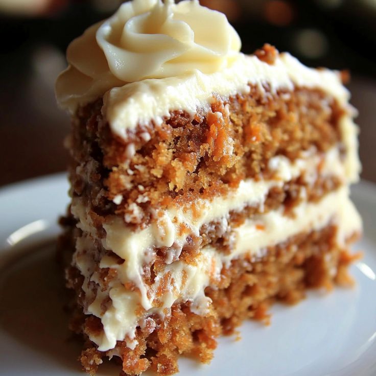 a piece of carrot cake with white frosting and nuts on top sits on a plate