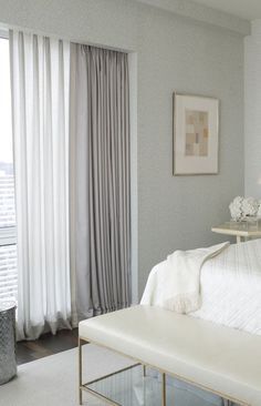 a white bed sitting in a bedroom next to a window with curtains on the windowsill