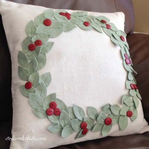 a white pillow with green leaves and red berries on it sitting on a brown chair