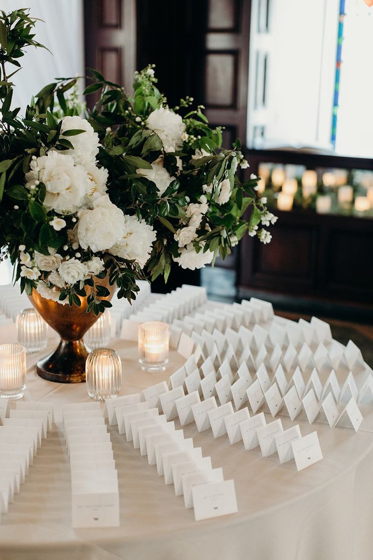 a vase filled with white flowers sitting on top of a table covered in place cards