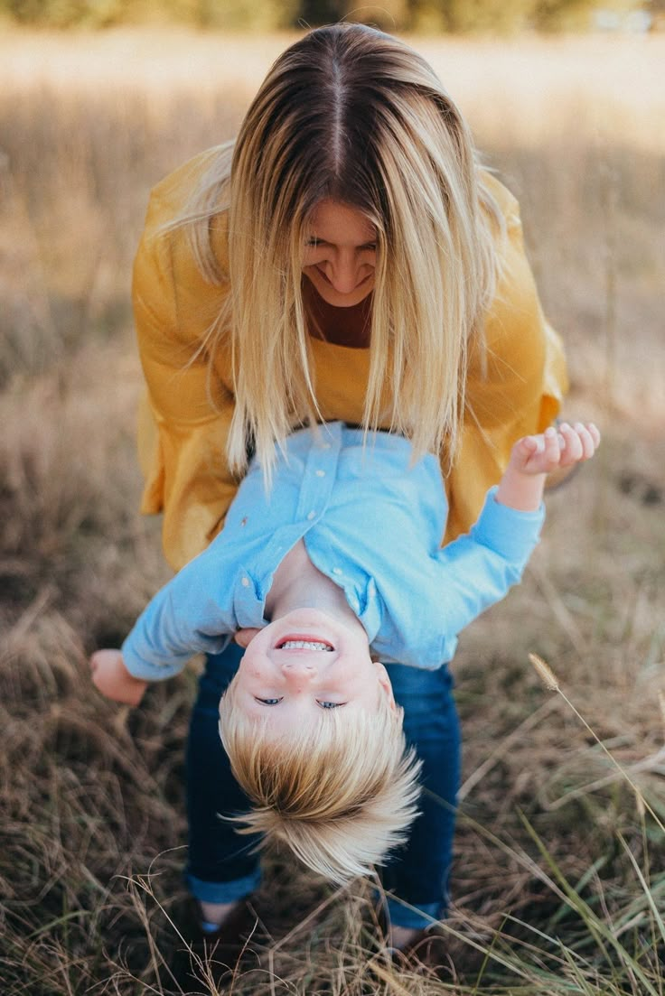 a woman is playing with a small child in the middle of some tall brown grass