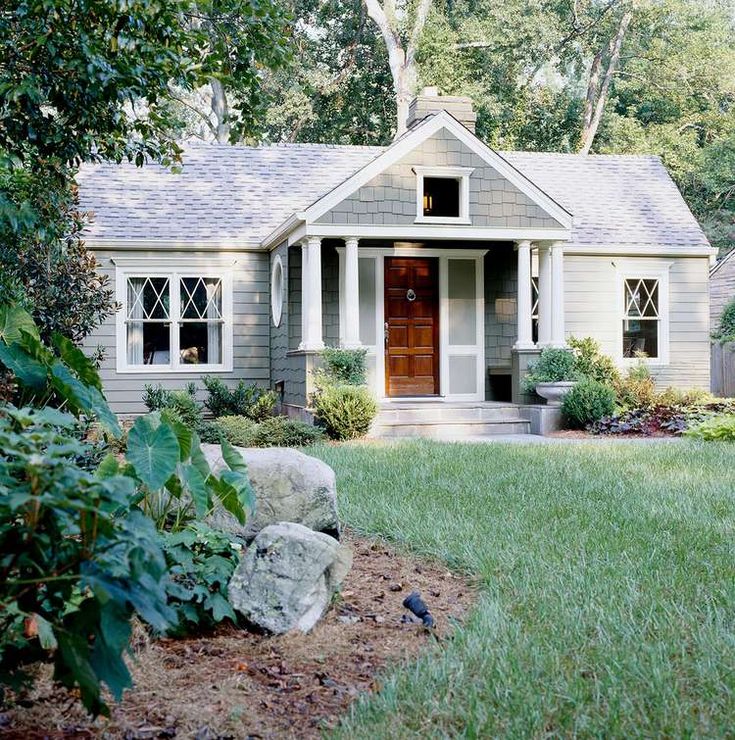 a small gray house sitting in the middle of a lush green yard