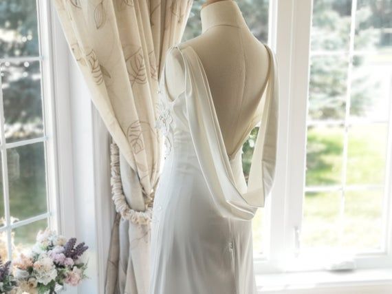 the back of a wedding dress hanging on a mannequin in front of a window