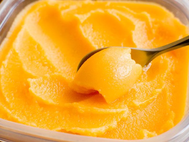 a plastic container filled with orange custard and a spoon full of ice cream