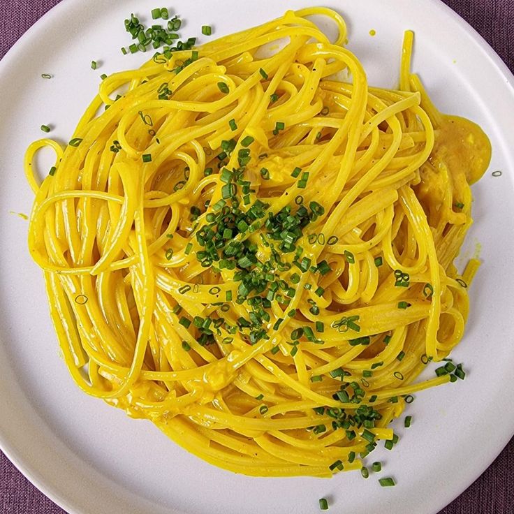 a white plate topped with yellow pasta and garnished with green pepper sprinkles