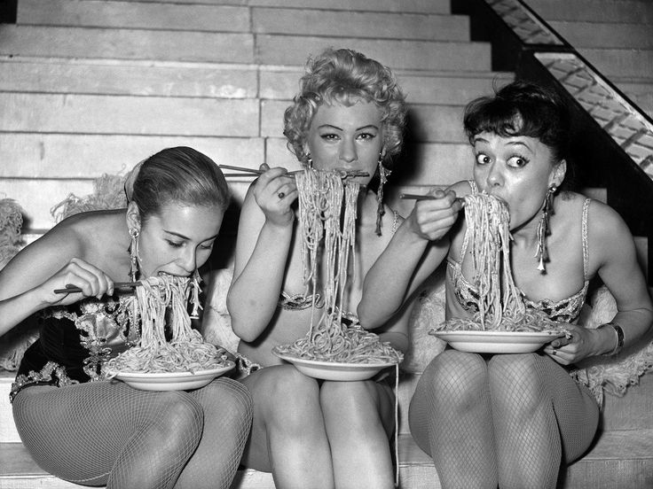 three women are eating spaghetti together on the stairs