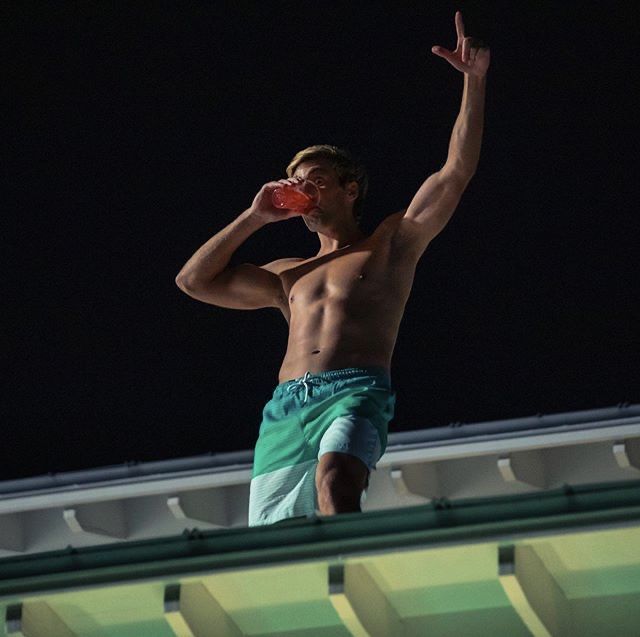 a shirtless man drinking from a water bottle on top of a roof at night