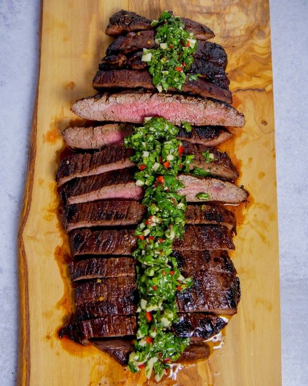 a wooden cutting board topped with sliced up steak and garnished with green sauce