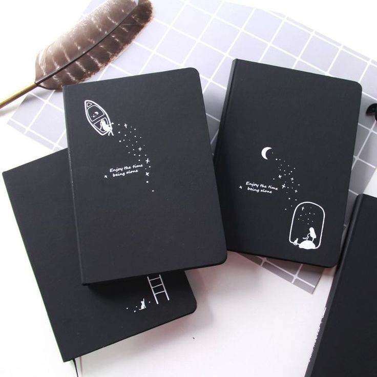 three black notebooks sitting on top of a table next to an open feather quill