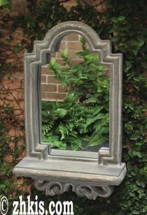 a mirror sitting on top of a stone shelf next to a wall covered in green plants