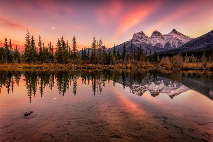 a mountain range is reflected in the still waters of a lake as the sun sets