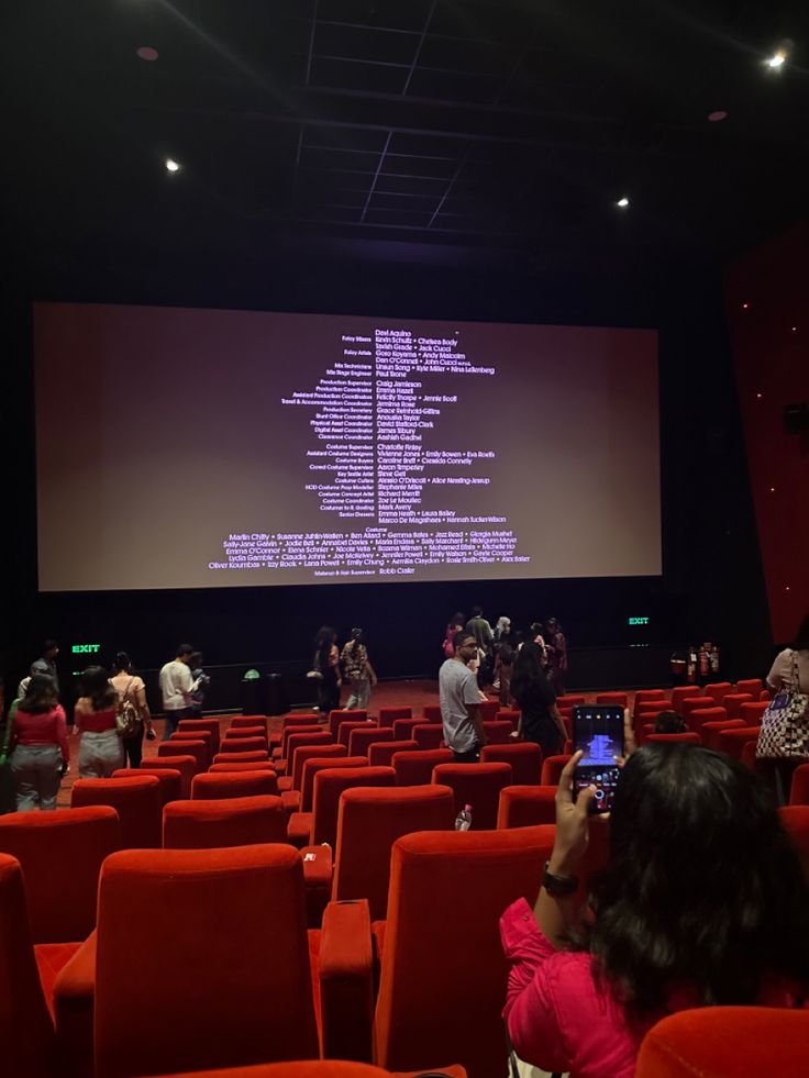 people are taking pictures in front of a large screen at an auditorium with red chairs