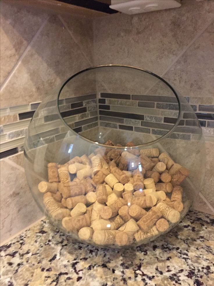 a glass bowl filled with wine corks on top of a marble counter next to a tile backsplash