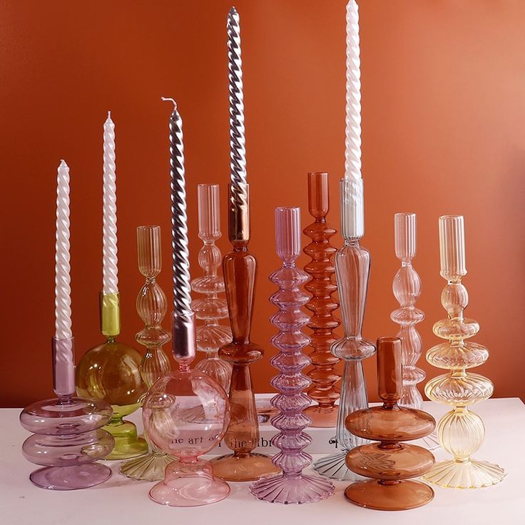 there are many different colored glass vases and candles on the table in front of an orange wall