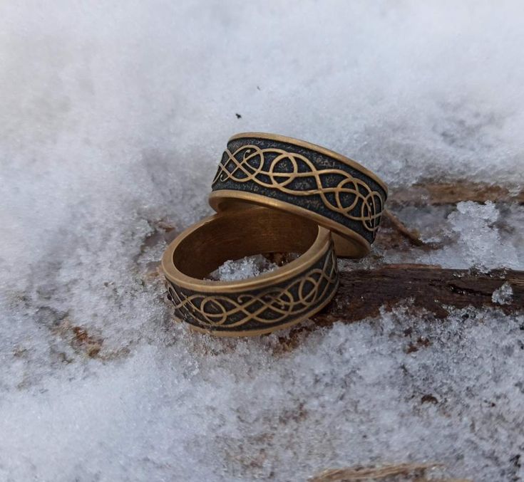 two rings sitting in the snow on top of some snow covered ground and one has an intricate design on it