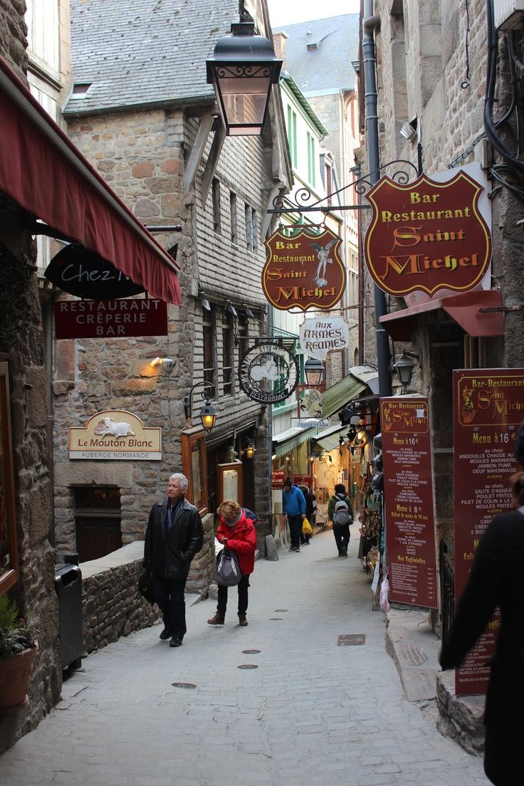 people are walking down an alley way in the old part of town with shops and restaurants