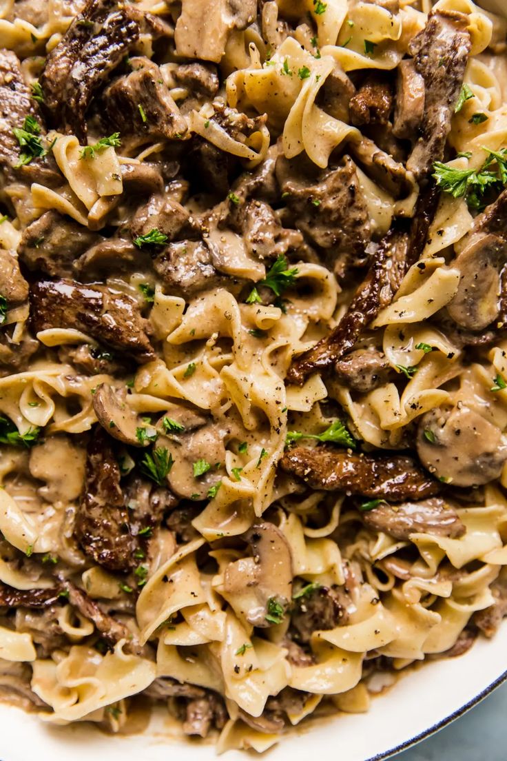 a bowl filled with pasta and meat covered in mushroom sauce, garnished with parsley