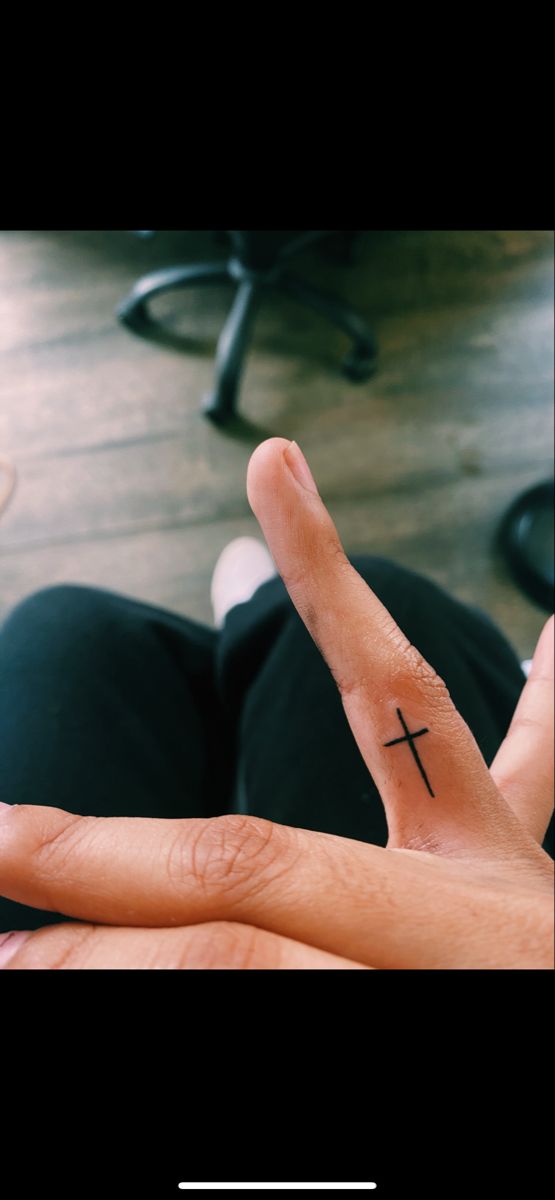 a person's hand with a small cross tattoo on the middle finger and fingers