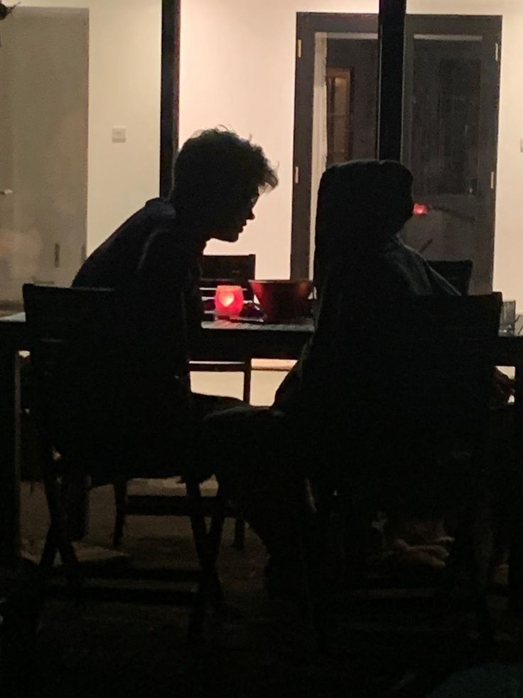 two people sitting at a table in front of a window with a red light on it