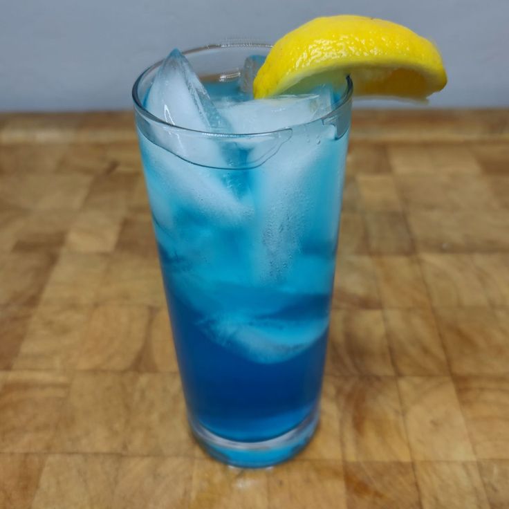 a blue drink with ice and a lemon wedge