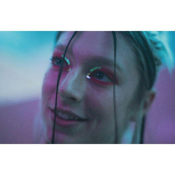 a woman with red eyes and pink makeup looks at the camera while holding her hair in front of her face