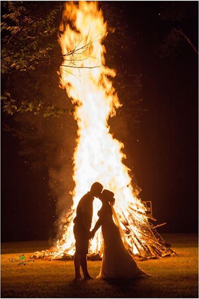 a bride and groom standing in front of a fire