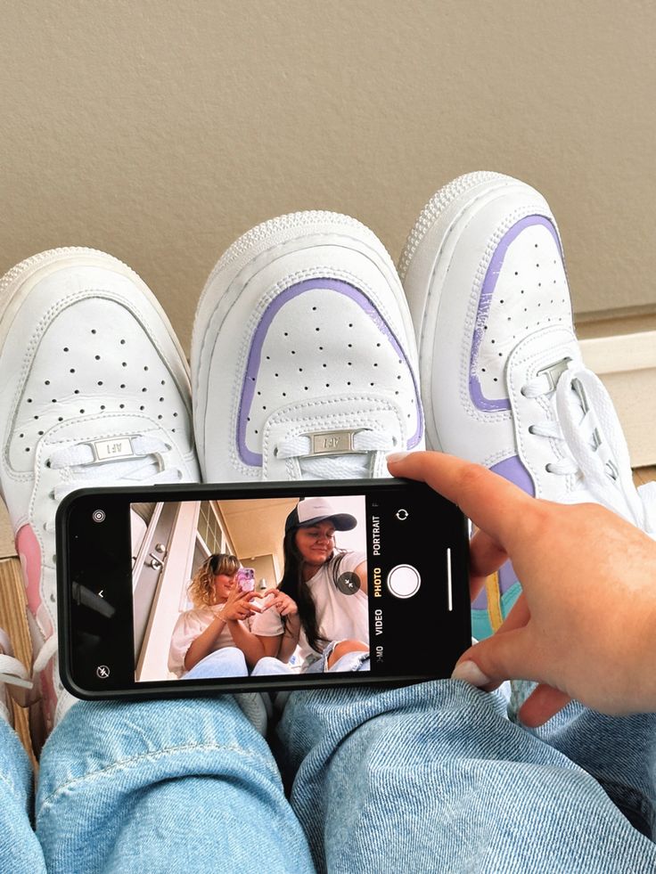 a person taking a photo with their cell phone in front of two pairs of shoes