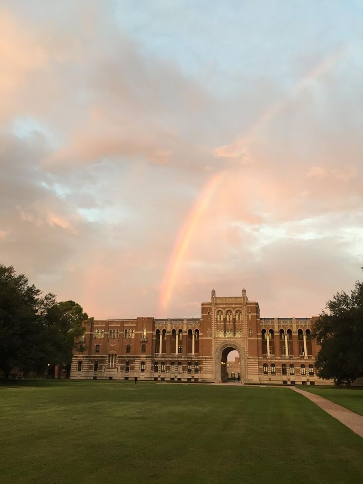 a rainbow shines in the sky over a large building with a green lawn and trees