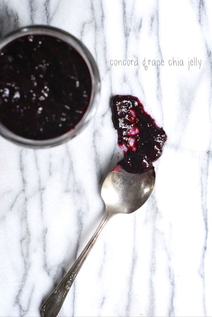 a spoon with blueberry sauce on it next to a bowl full of fruit jam