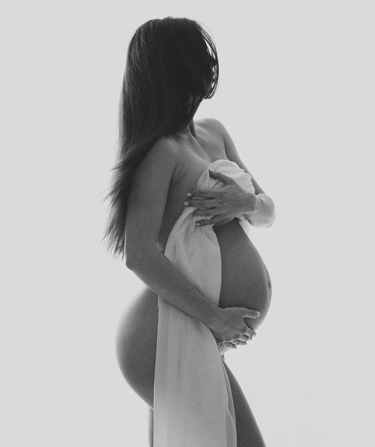 a pregnant woman wearing a white robe and holding her belly in front of the camera