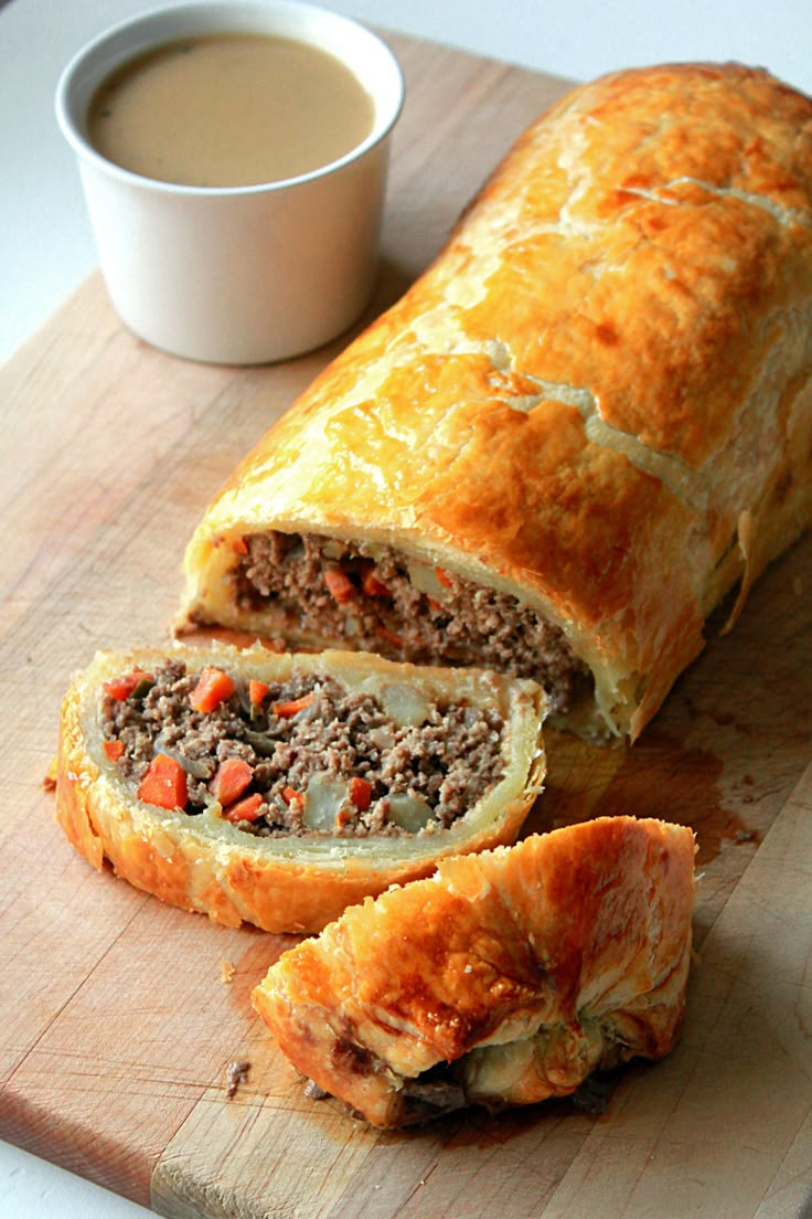 a meat and cheese roll cut in half on a cutting board next to a cup of coffee