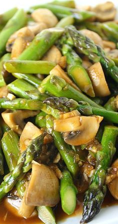 a white plate topped with asparagus, mushrooms and broccoli covered in sauce