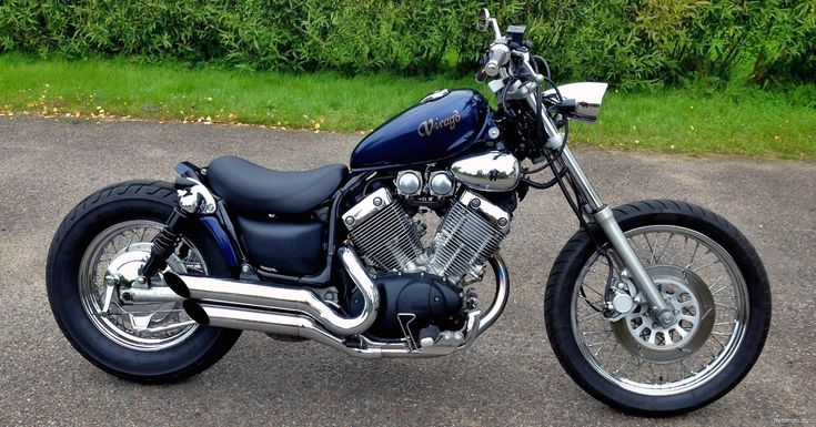 a blue motorcycle parked on top of a parking lot next to green grass and bushes