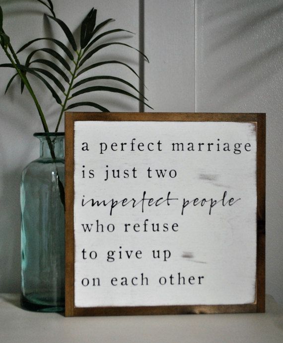 a wooden sign sitting on top of a table next to a vase filled with plants