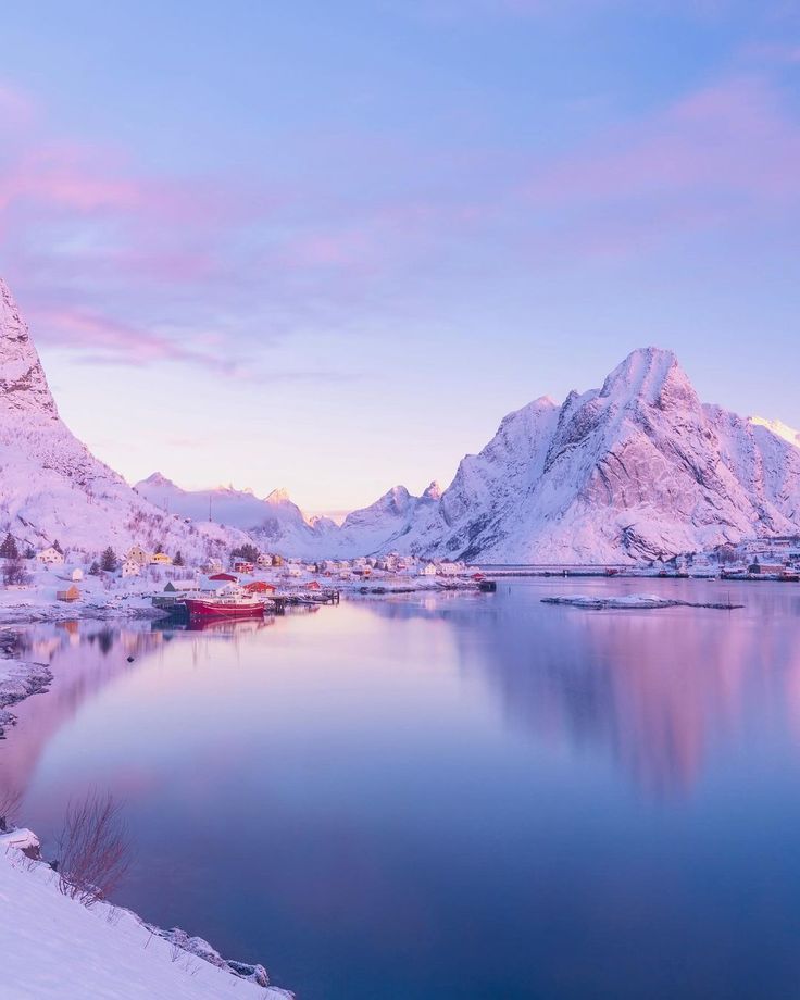 a lake surrounded by snow covered mountains in the middle of winter with a red boat on it