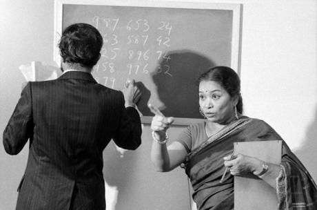 a woman standing in front of a blackboard with writing on it and another person holding papers