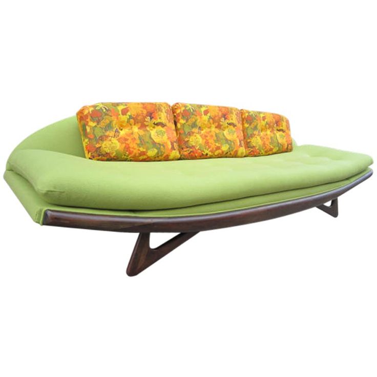 a green couch sitting on top of a wooden table next to a white wall with an orange and yellow pillow