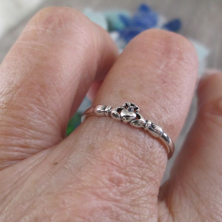 a person's hand with a silver ring on top of their finger and the other hand holding an animal paw