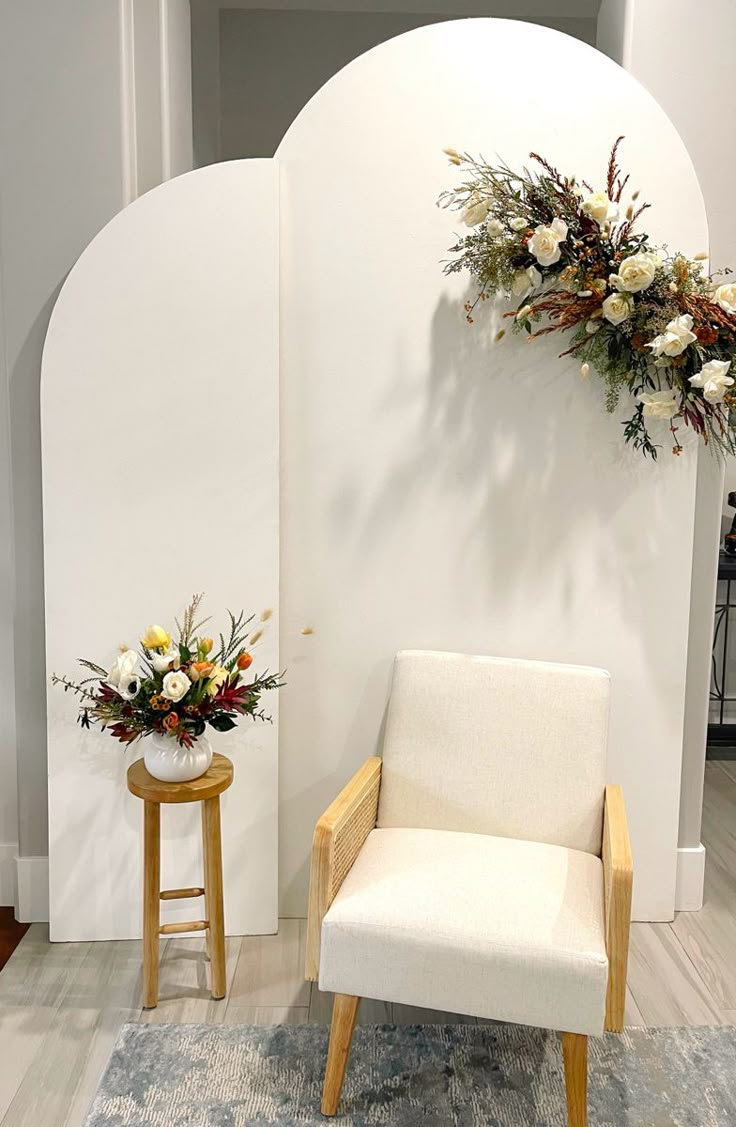 a white chair sitting on top of a wooden floor next to a vase filled with flowers