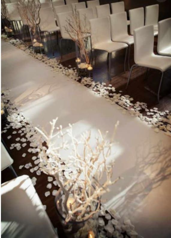 a room filled with lots of white chairs next to a table covered in flowers and branches